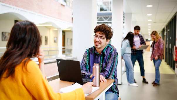 Student achter laptop in gesprek met andere student