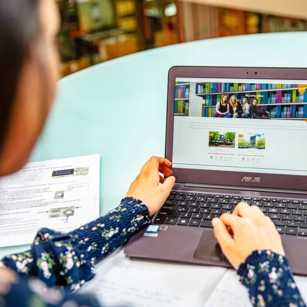 Student achter laptop met book your room app