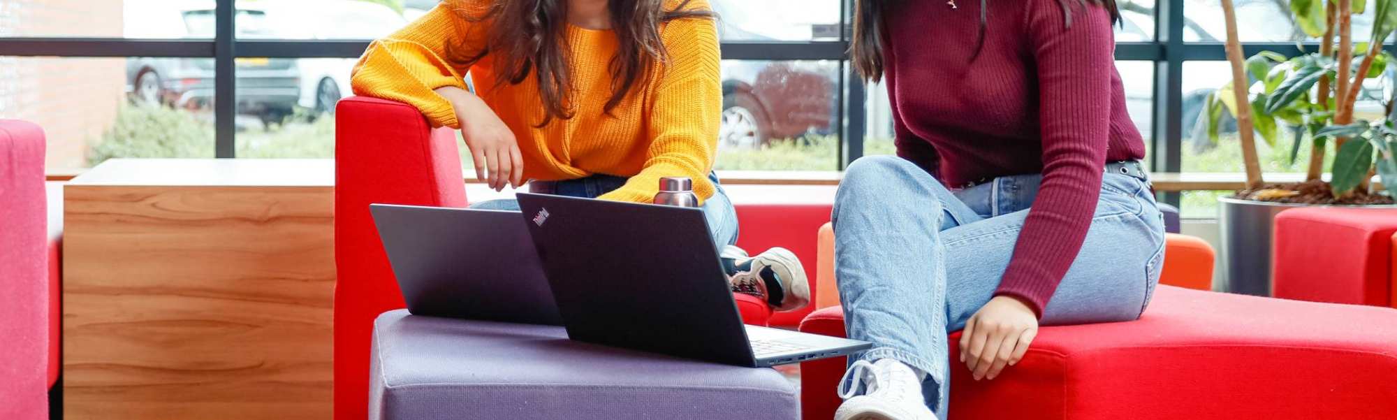 Twee internationael studenten overleggen met laptop bij rode banken