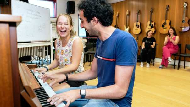 Twee studenten spelen op piano in muzieklokaal