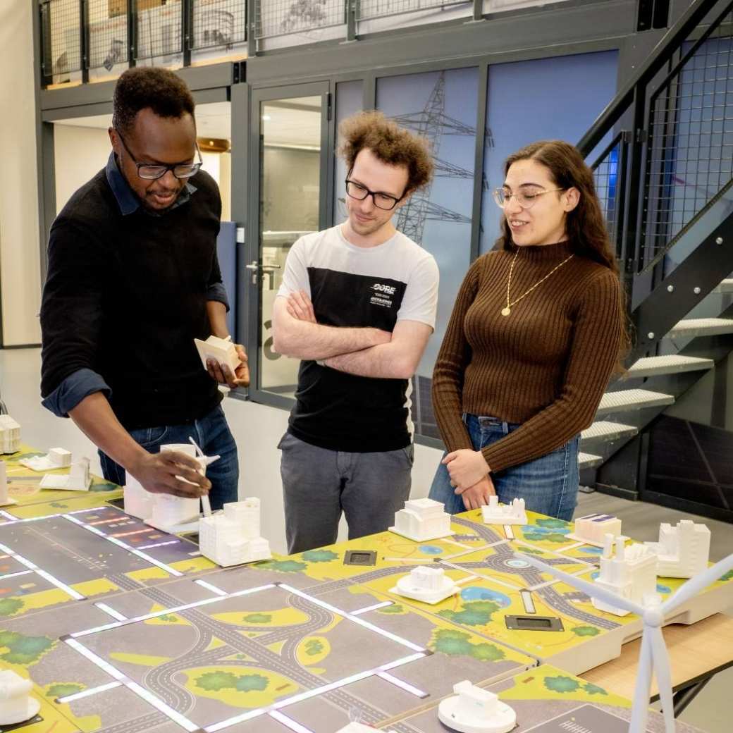 Twee studenten van de Master Engineering Systems Sustainable Energy en een docent bij de Smart Grid-demotafel.