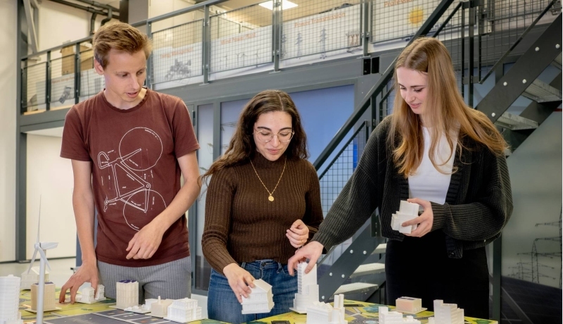 Drie studenten van de Master Engineering Systems Sustainable Energy werken aan de Smart Grid-tafel.