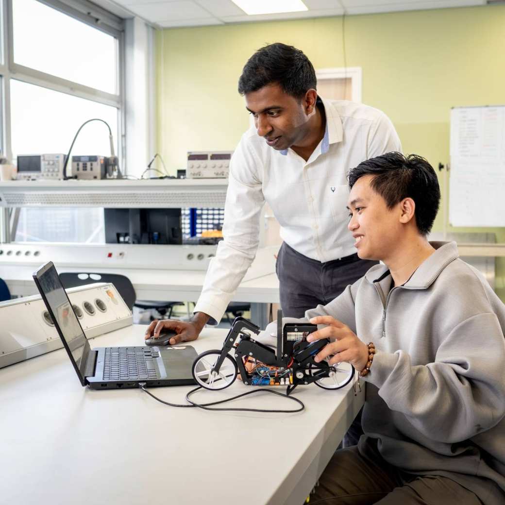 Een docent van de Master Engineering Systems Cyber Physical Systems kijkt mee op de pc van een student.