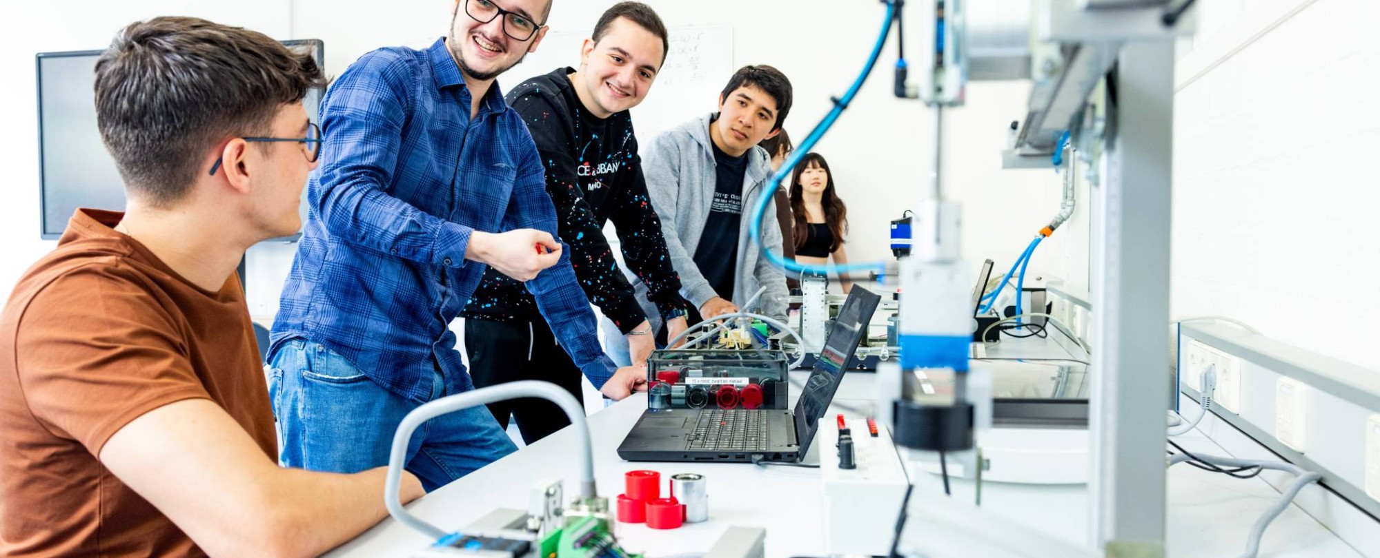 Docent en studenten elektrotechniek  aan een Programmable Logic Controller (PLC).