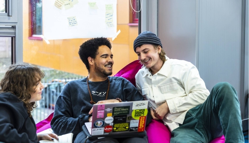 International Social Work. Drie studenten in gesprek. De middelste heeft een laptop. Ze zitten er relaxt bij.