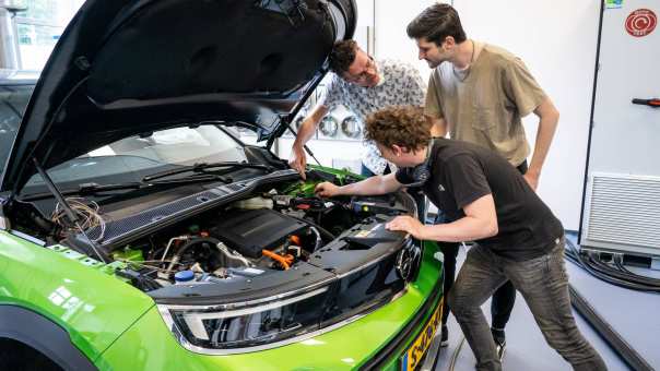 Studenten en docent automotive kijken naar de motor van de auto.