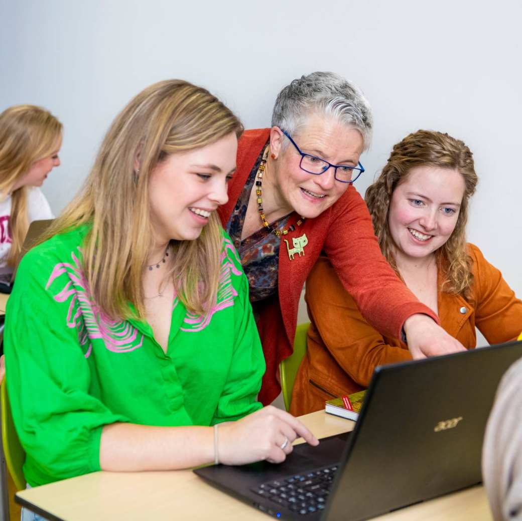 Lerarenopleider helpt twee studenten door iets aan te wijzen op de laptop die voor hun staat.
