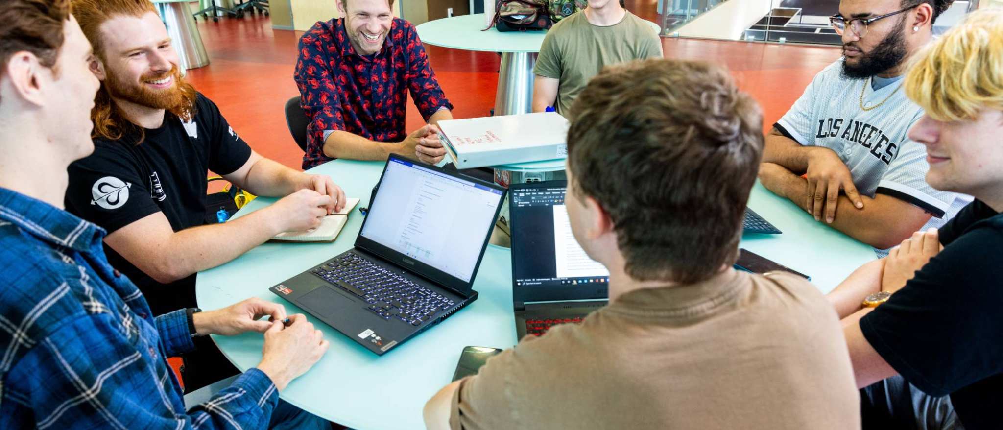 a group of engineering students -mechanical werktuigbouwkunde - working on a project together at a round table with laptops