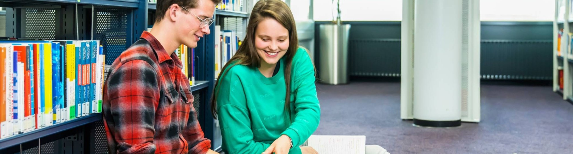 jongen en meisje studeren samen op de grond in studiecentrum en zij wijst iets aan