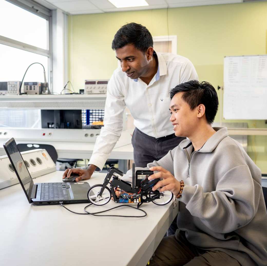 Een docent van de Master Engineering Systems Cyber Physical Systems kijkt mee op de pc van een student.