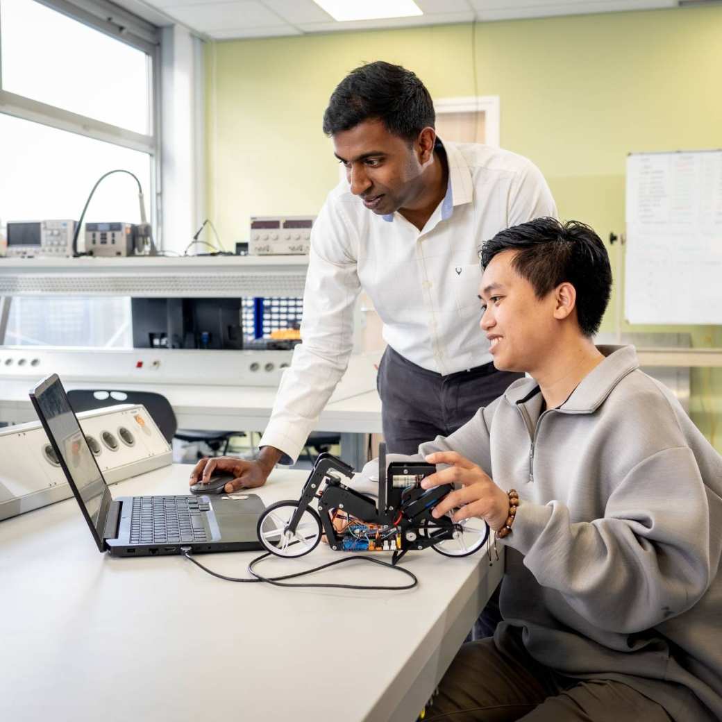 Een docent van de Master Engineering Systems Cyber Physical Systems kijkt mee op de pc van een student.