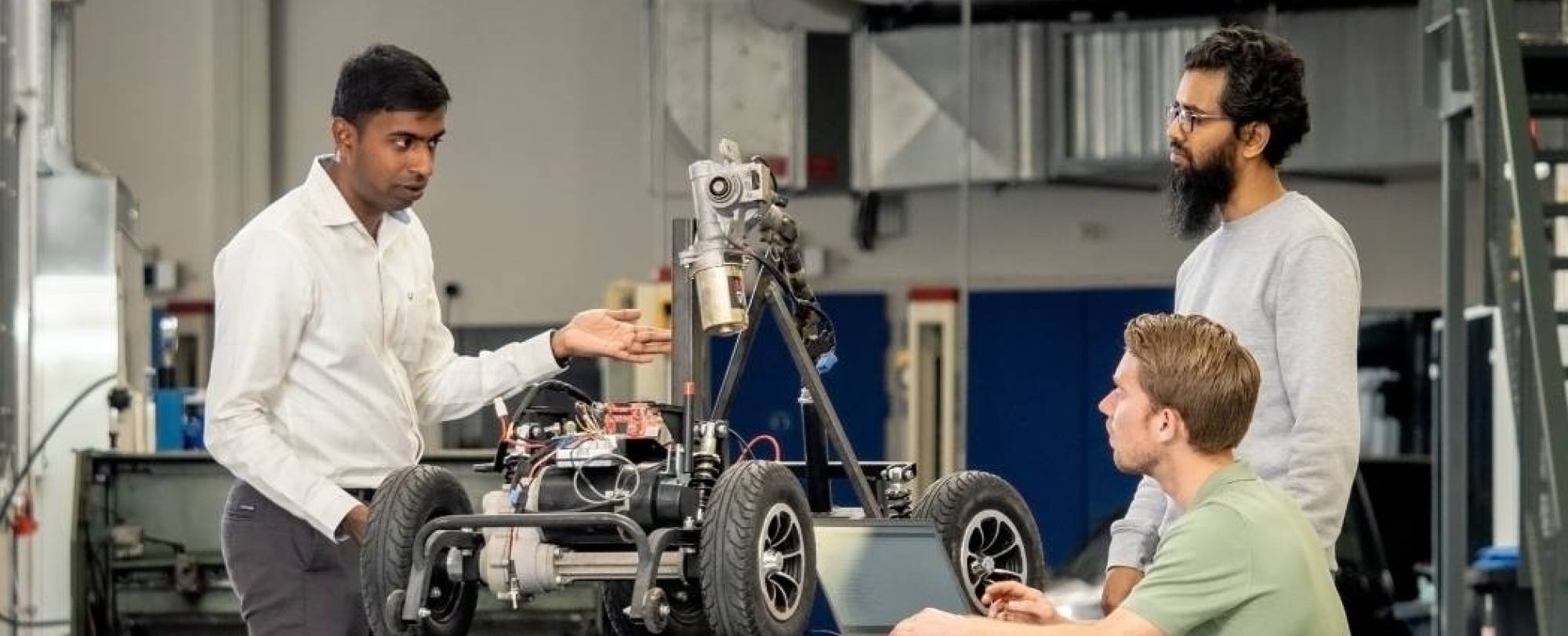 Een docent van de Master Engineering Systems Cyber Physical Systems staat met twee studenten bij het MORE-project, de scootmobiel.