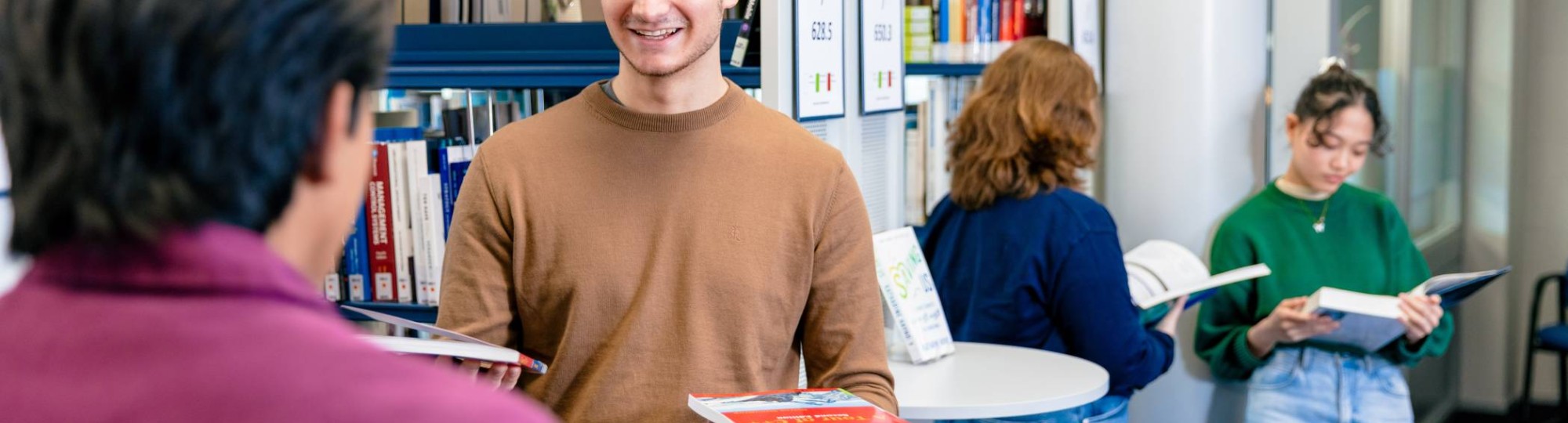 International students Diego, Andrei, Noa and Tam browsing through books in the library on the Arnhem campus of HAN University of Applied Sciences.