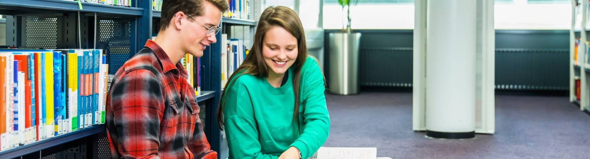 jongen en meisje studeren samen op de grond in studiecentrum en zij wijst iets aan