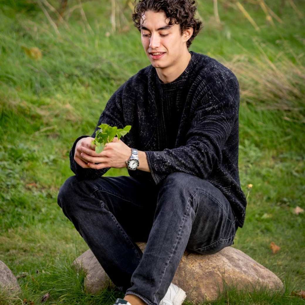 Paulino sits on a stone and looks at a plant. Photography: Linda Verweij