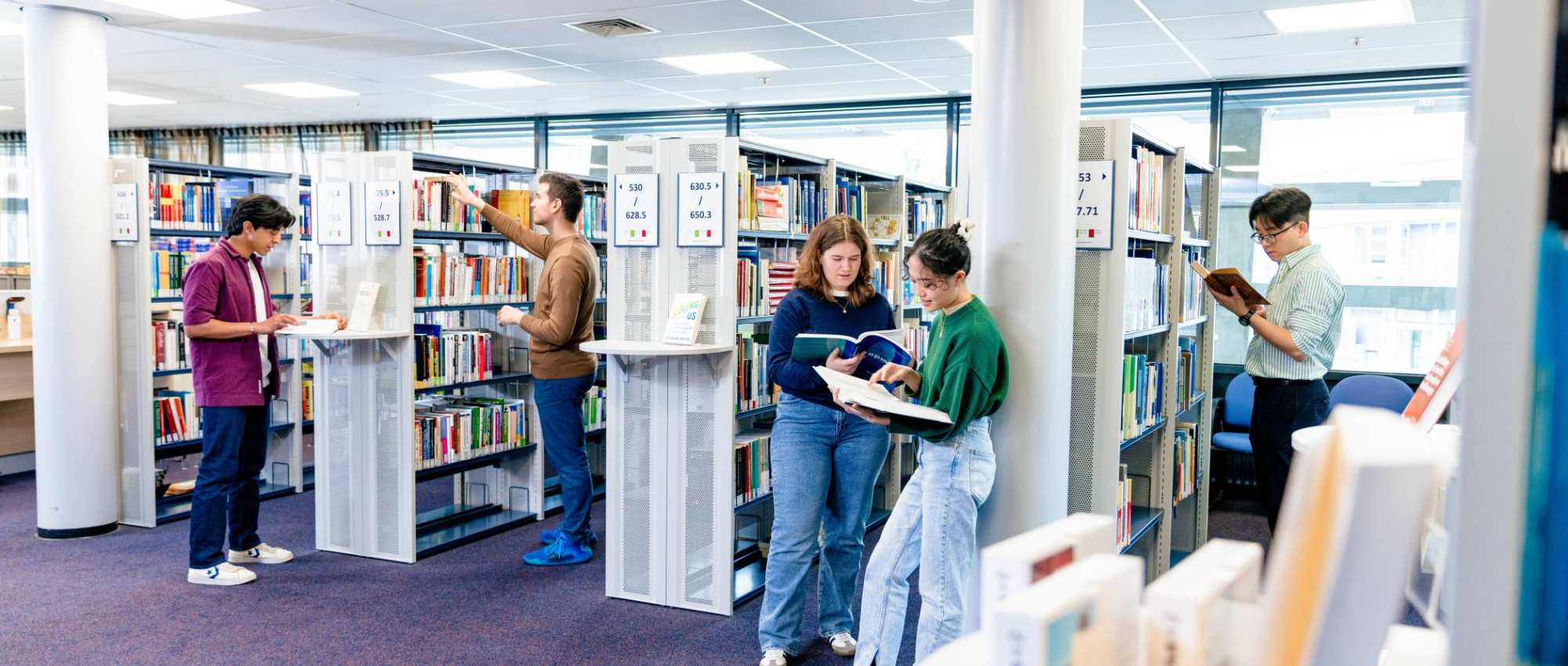 International students browsing through study books in the library on the Arnhem campus of HAN University of Applied Sciences.