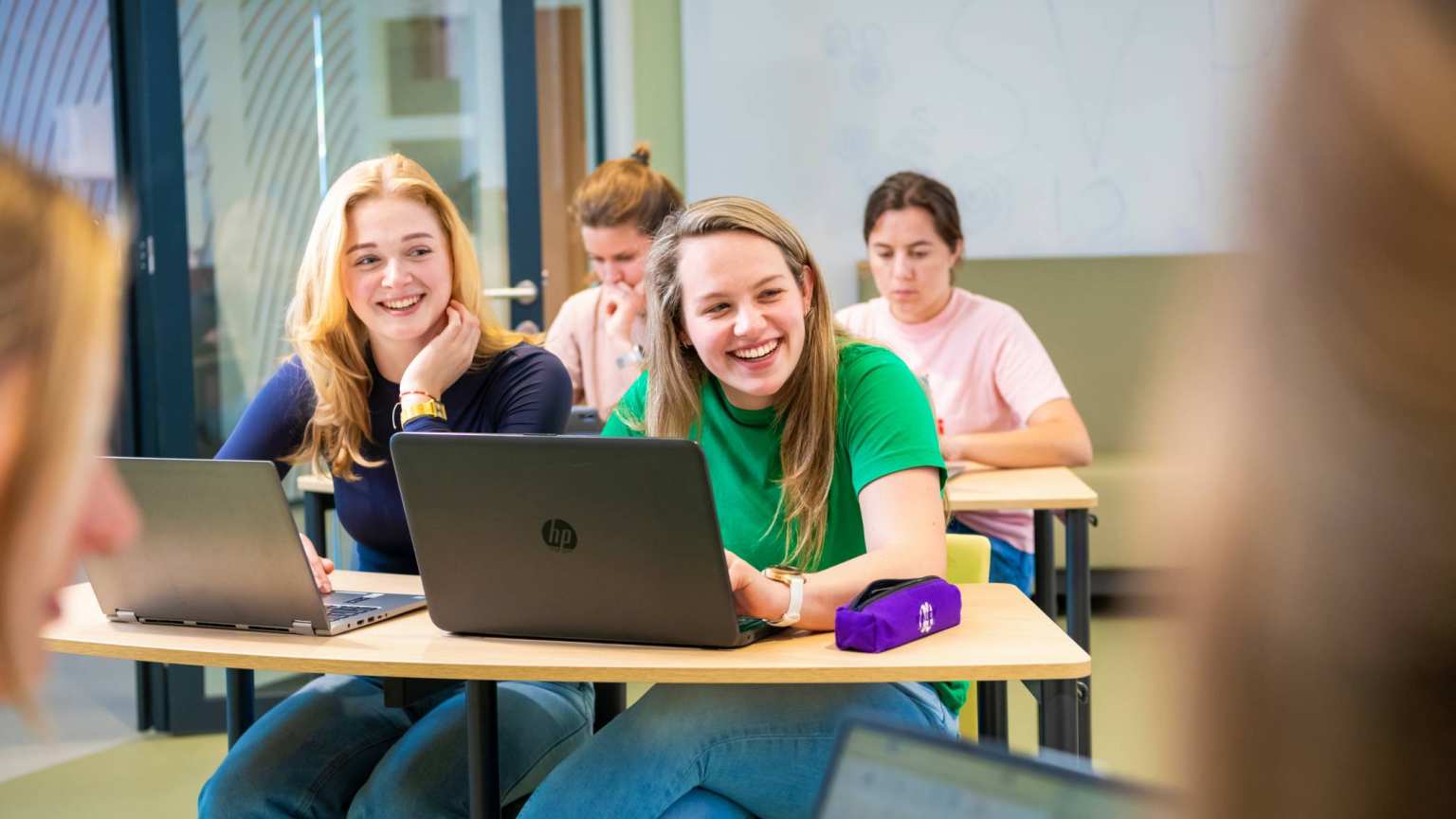 Studenten tijdens theorieles lachend achter laptops