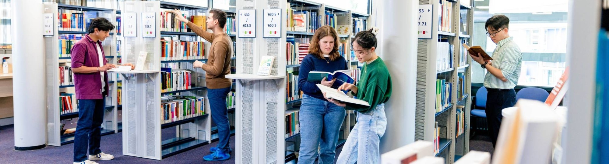 International students browsing through study books in the library on the Arnhem campus of HAN University of Applied Sciences.