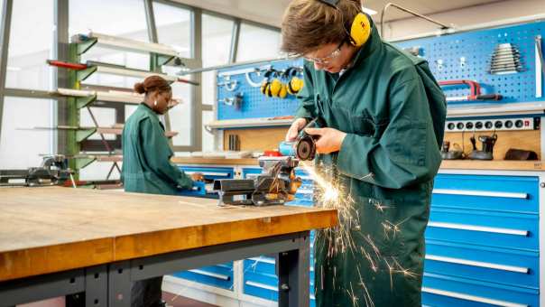 Een werktuigbouwkunde student slijpt een metalen staaf op maat.