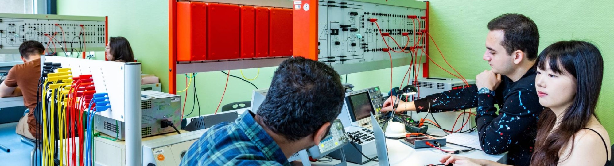 Een elektrotechniekdocent kijkt mee met studenten tijdens practicum.