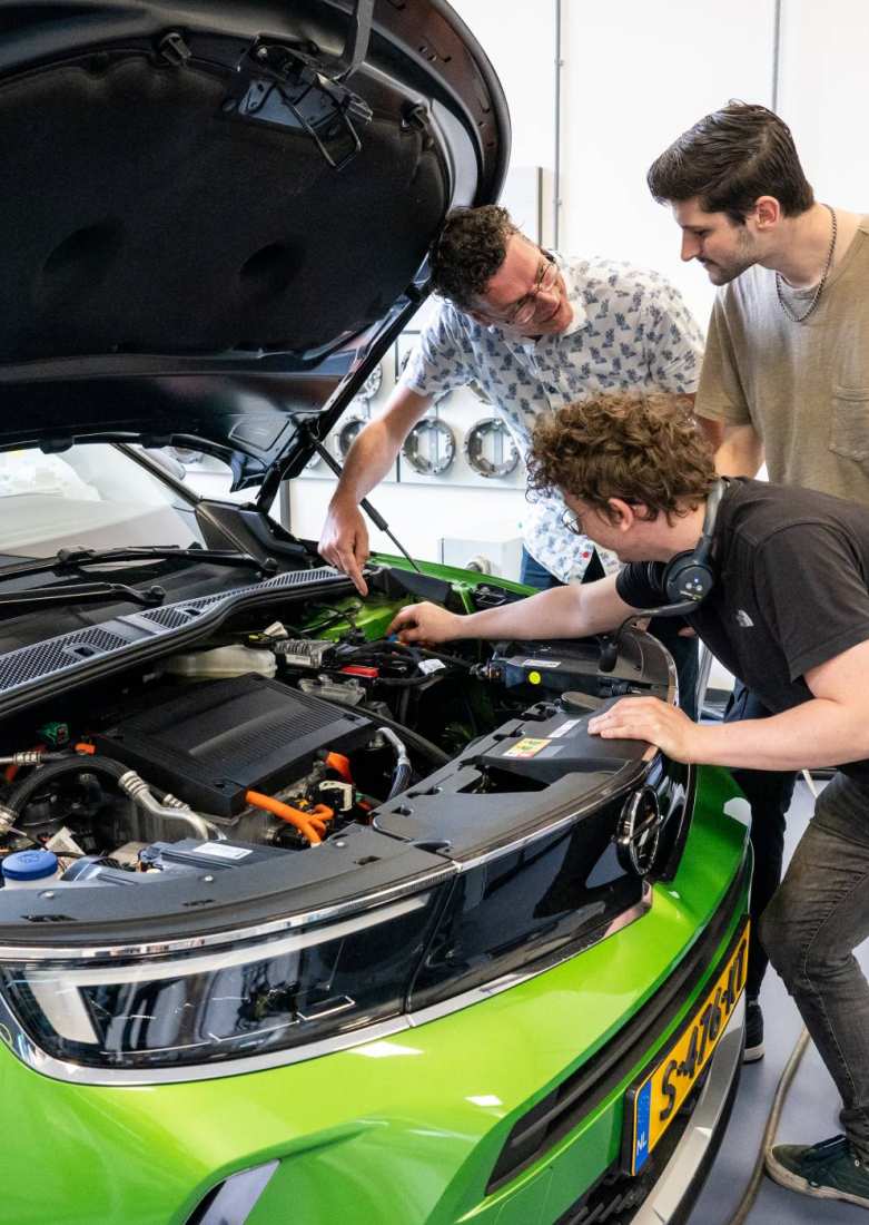 Studenten en docent automotive kijken naar de motor van de auto.