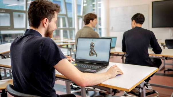 Een student werktuigbouwkunde 3D-tekent op zijn laptop in het klaslokaal.