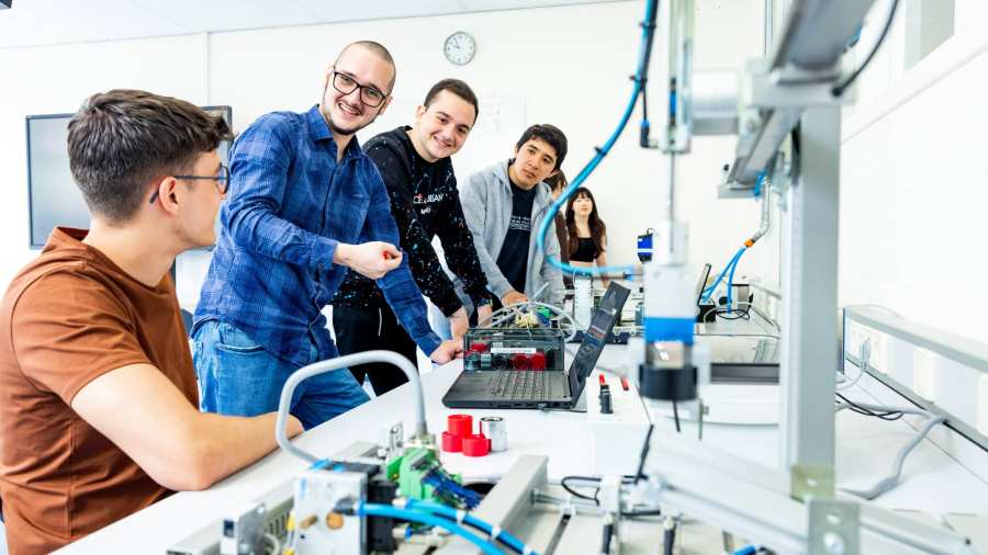 Docent en studenten elektrotechniek  aan een Programmable Logic Controller (PLC).