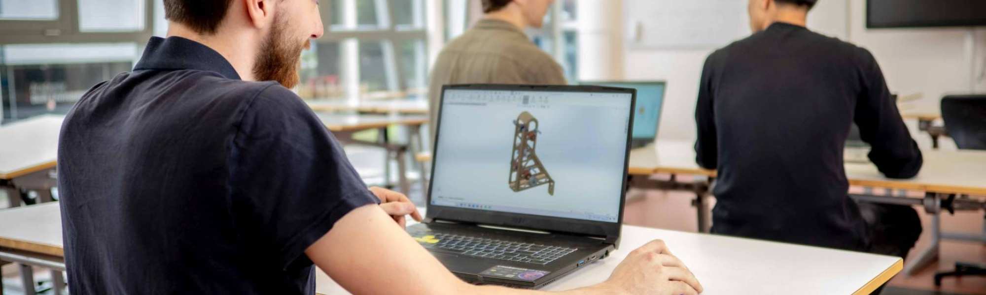 Een student werktuigbouwkunde 3D-tekent op zijn laptop in het klaslokaal.