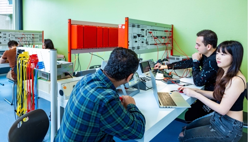 Een elektrotechniekdocent kijkt mee met studenten tijdens practicum.